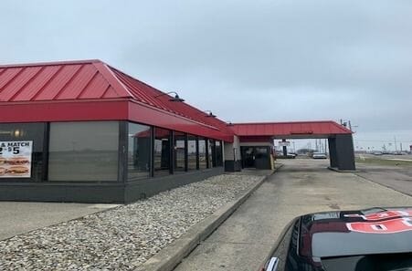 Commercial building with red metal roof and gray exterior walls on cloudy day