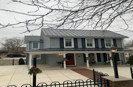 Modern two-story house with green siding and metal roof on overcast day