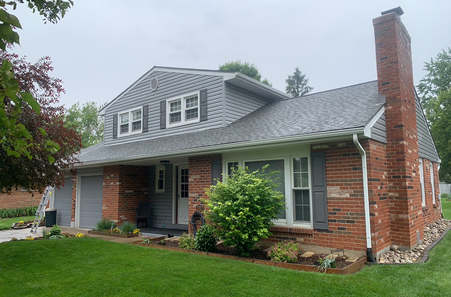 Red brick ranch house with dormer windows and chimney on manicured lawn