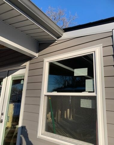 Gray house exterior with white-framed windows and gutters under blue sky