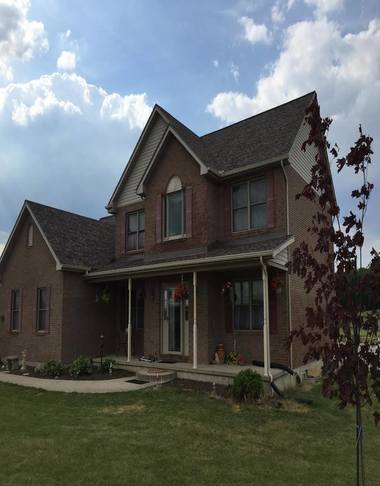 Two-story brick house with front porch and green lawn under cloudy blue sky