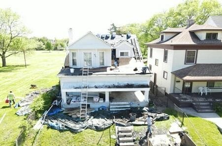 Aerial view of home roof replacement with workers installing new shingles and ladders