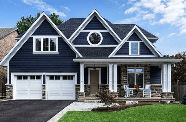 Modern blue and stone two-story house with white garage doors and front porch