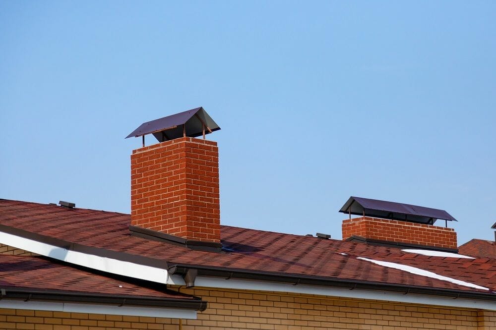 Red brick chimneys with metal caps on tiled roof against clear blue sky