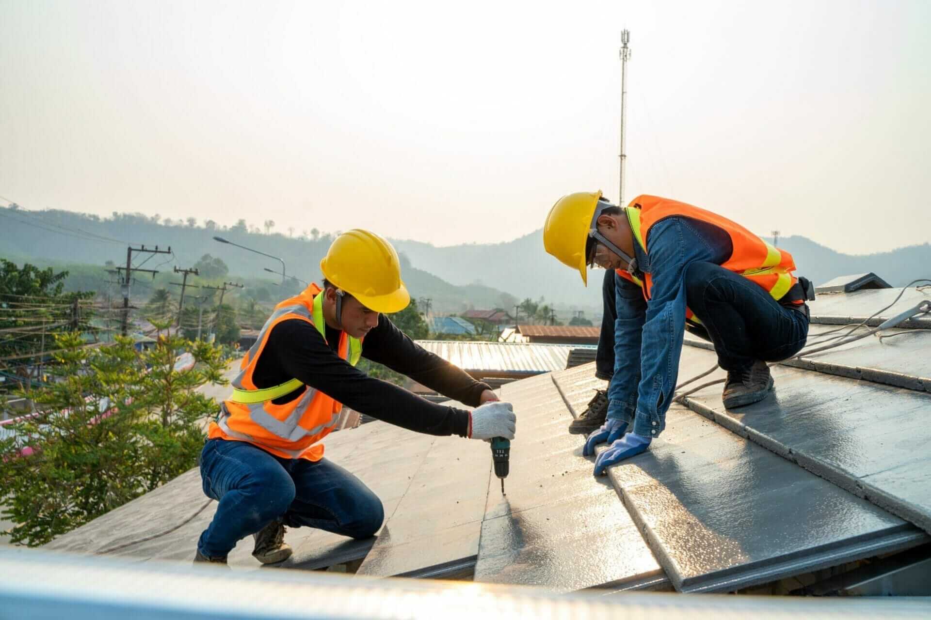 Two construction workers in safety gear installing solar panels on rooftop