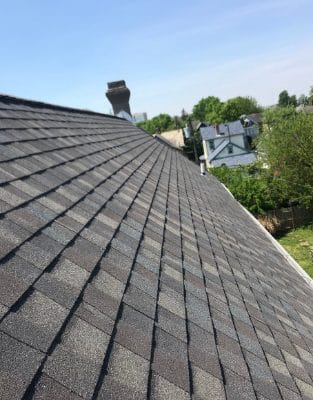 Gray asphalt shingle roof with chimney under blue sky in residential neighborhood