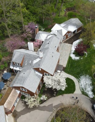 Aerial view of large residential home with gray roof surrounded by spring trees