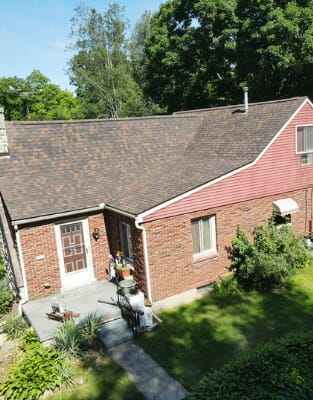 Aerial view of red brick ranch house with asphalt shingle roof and green lawn