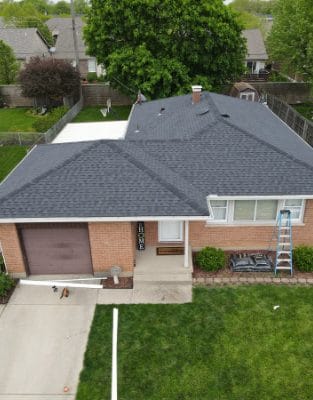 Aerial view of brick ranch home with gray asphalt shingle roof and driveway