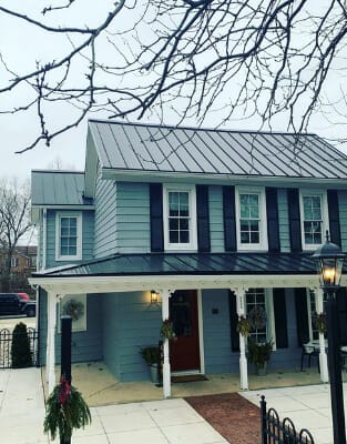 Charming green colonial house with metal roof and white columns on front porch