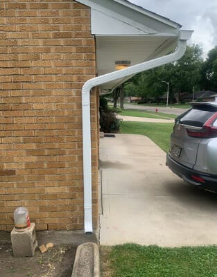 White gutter downspout installed on brick house exterior with concrete driveway