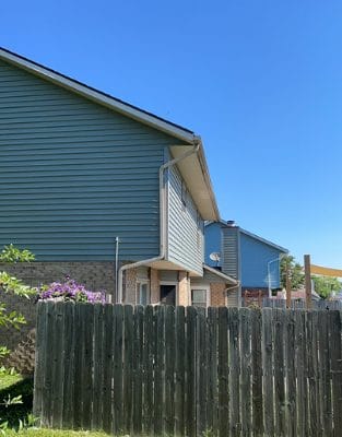 Modern suburban homes with gray siding behind wooden fence under clear blue sky