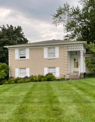 Two-story beige brick house with white trim and well-maintained lawn