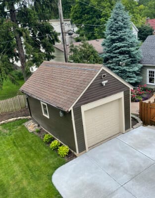 Green detached garage with brown shingle roof in residential backyard setting