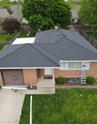 Aerial view of brick ranch home with gray asphalt shingle roof and attached garage