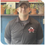 Man in dark polo shirt and cap standing in front of shelves with potted plants