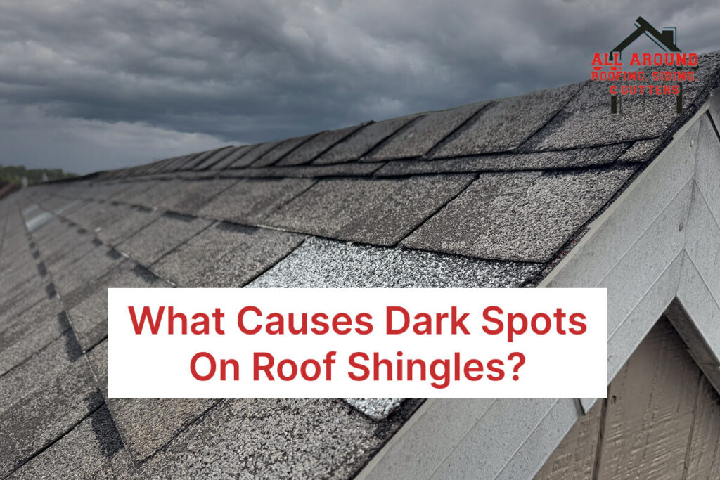Close-up of roof shingles with dark spots under a cloudy sky.