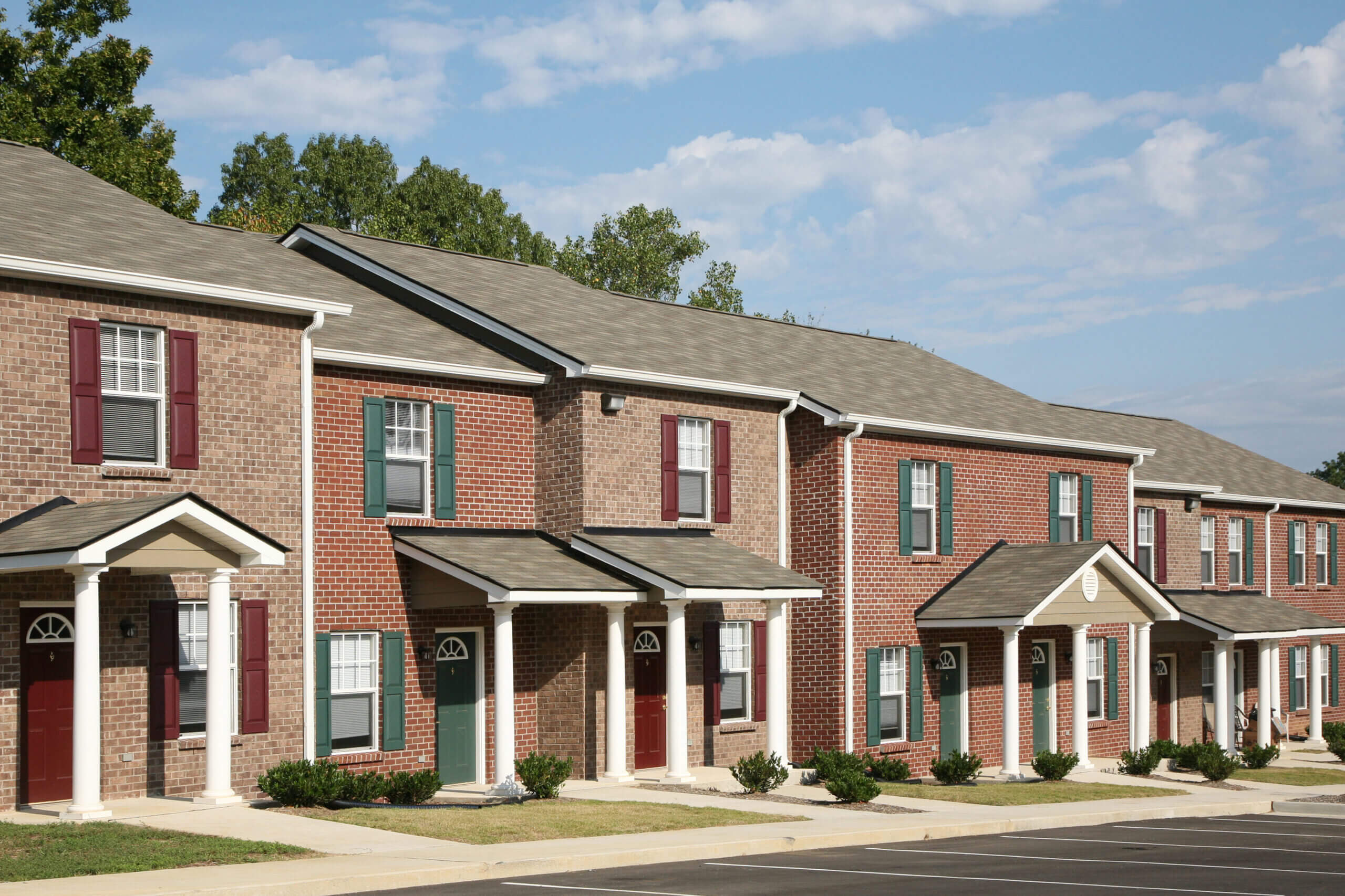Row of brick townhouses with colorful shutters and front porches on sunny day
