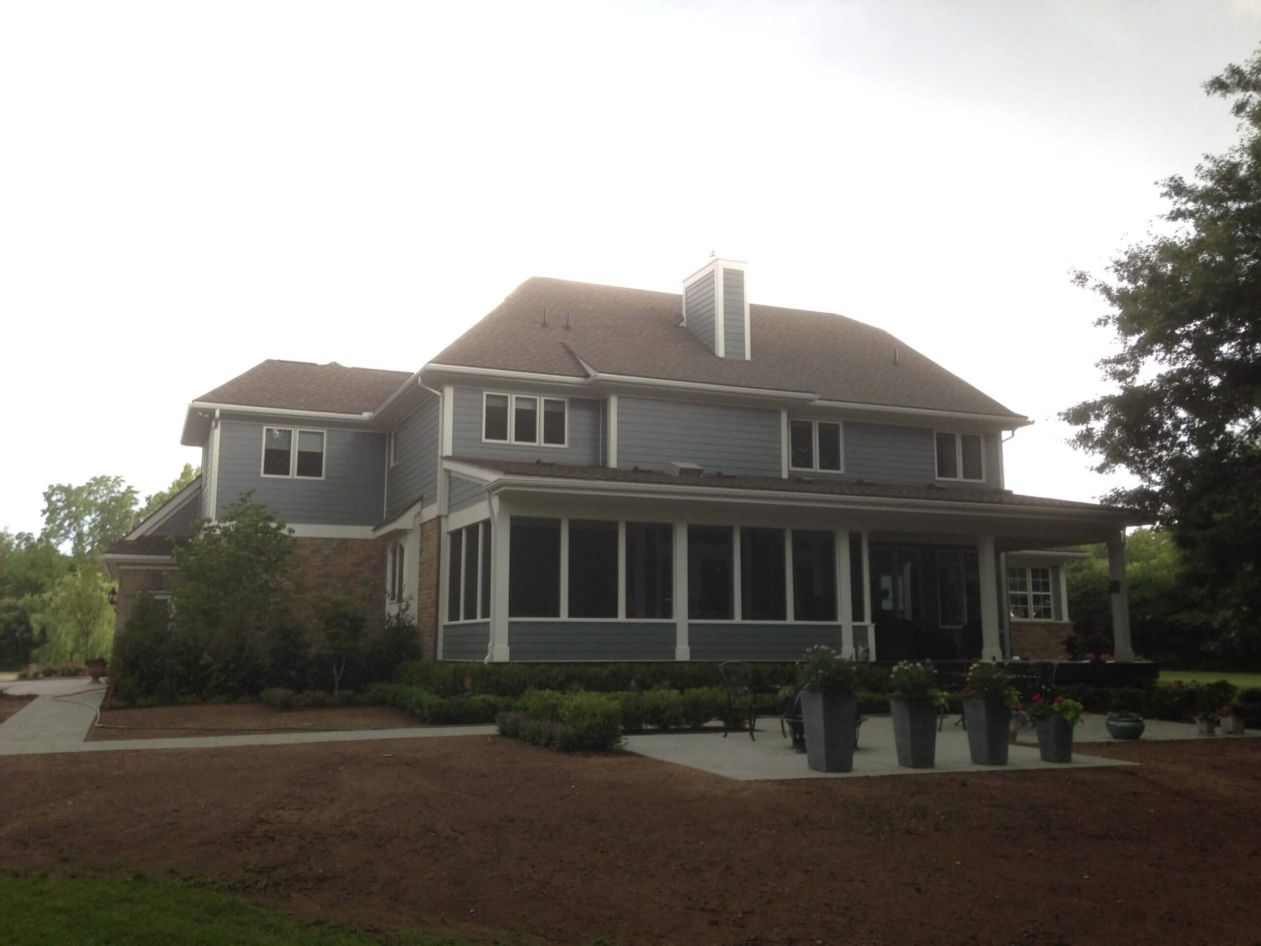 Two-story gray house with wraparound porch and white chimney in residential setting