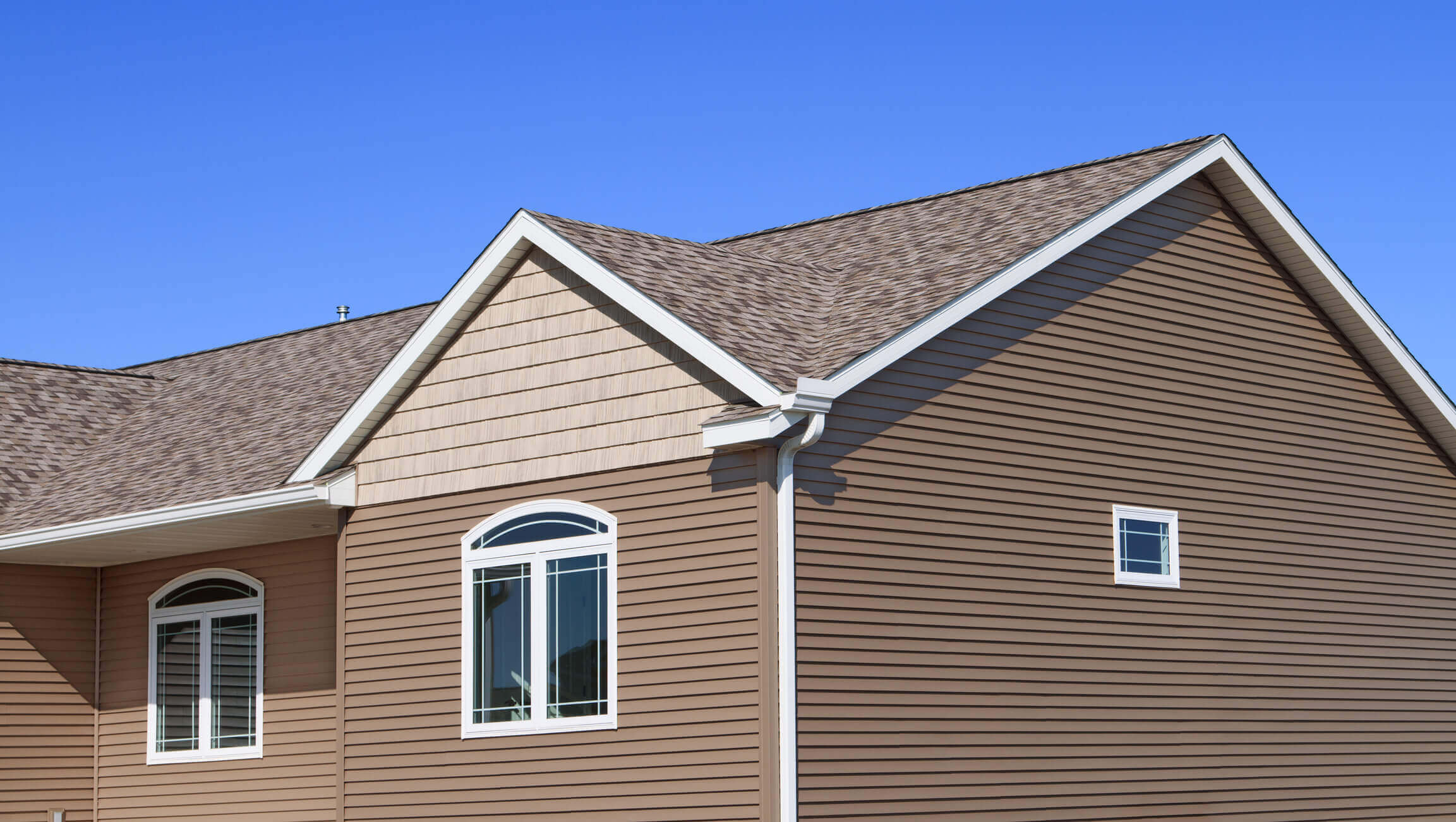 Modern beige house exterior with brown vinyl siding and white trim windows