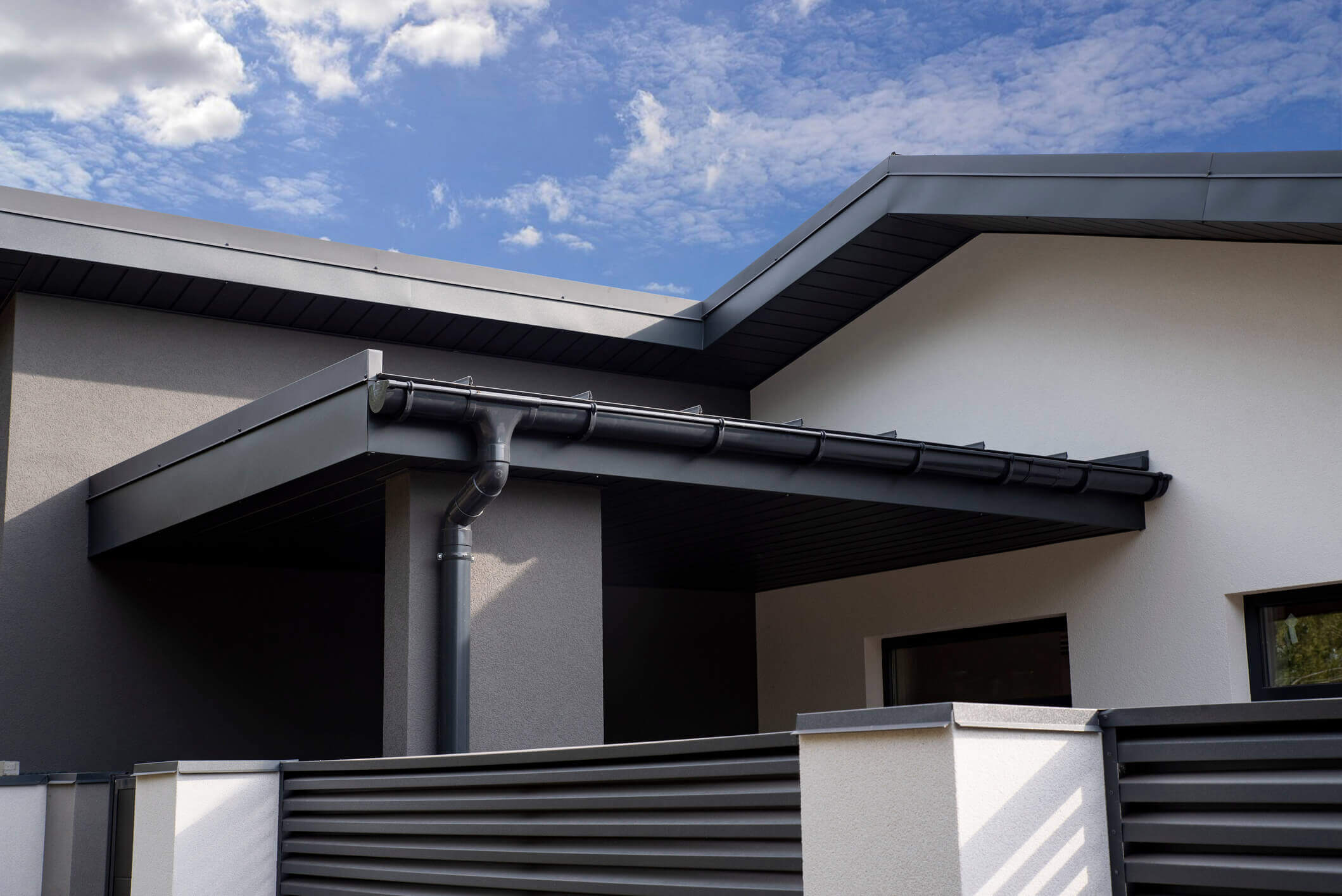 Modern house exterior with dark gutters and downspout against blue cloudy sky