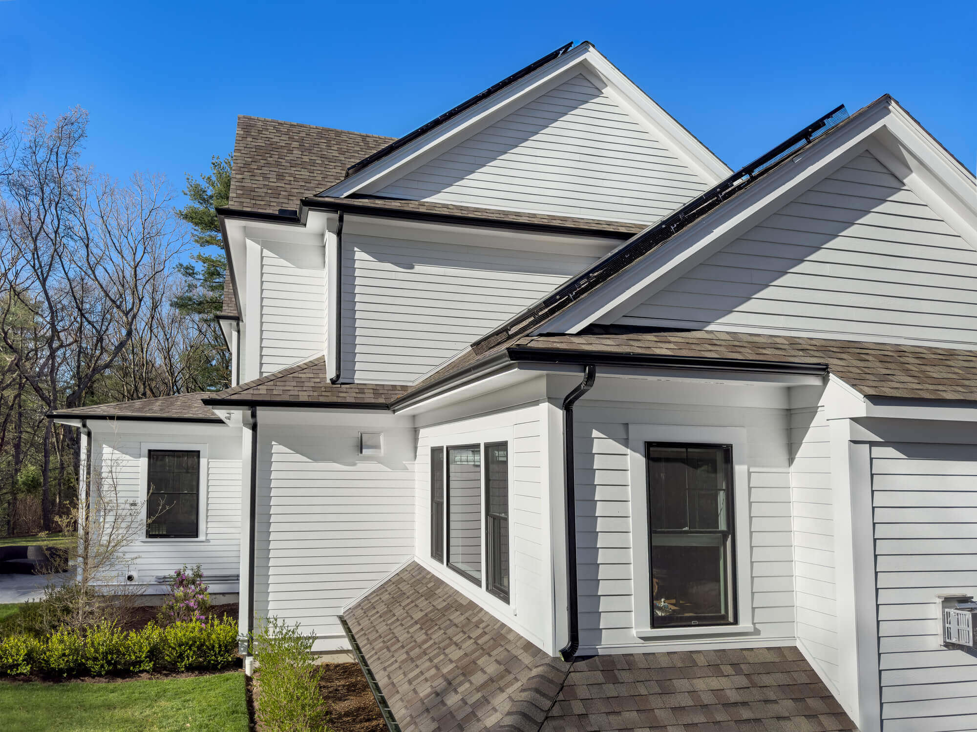 Modern white vinyl siding house with gray shingle roof against clear blue sky