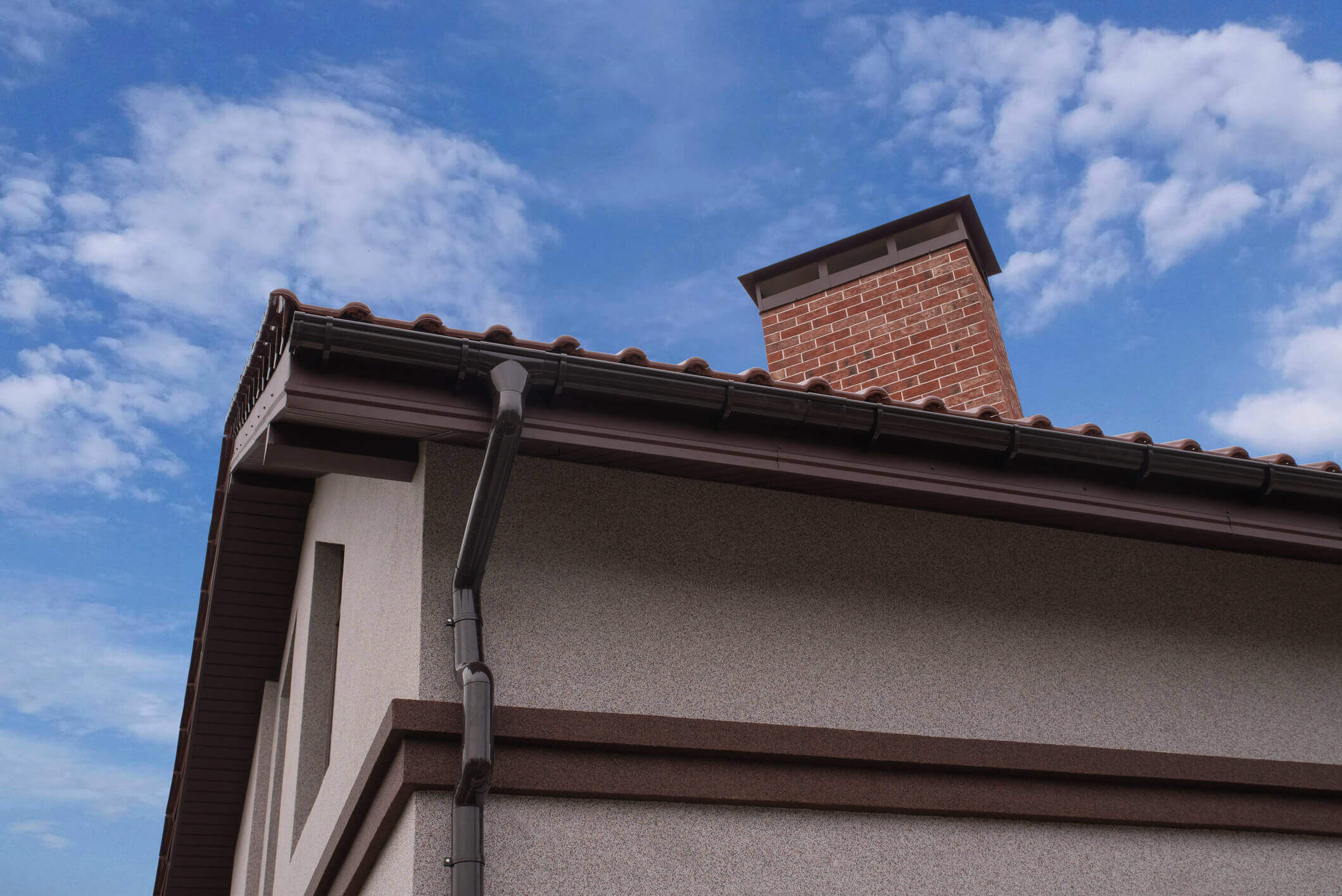 Modern house exterior with brick chimney, tile roof and gutters against blue sky