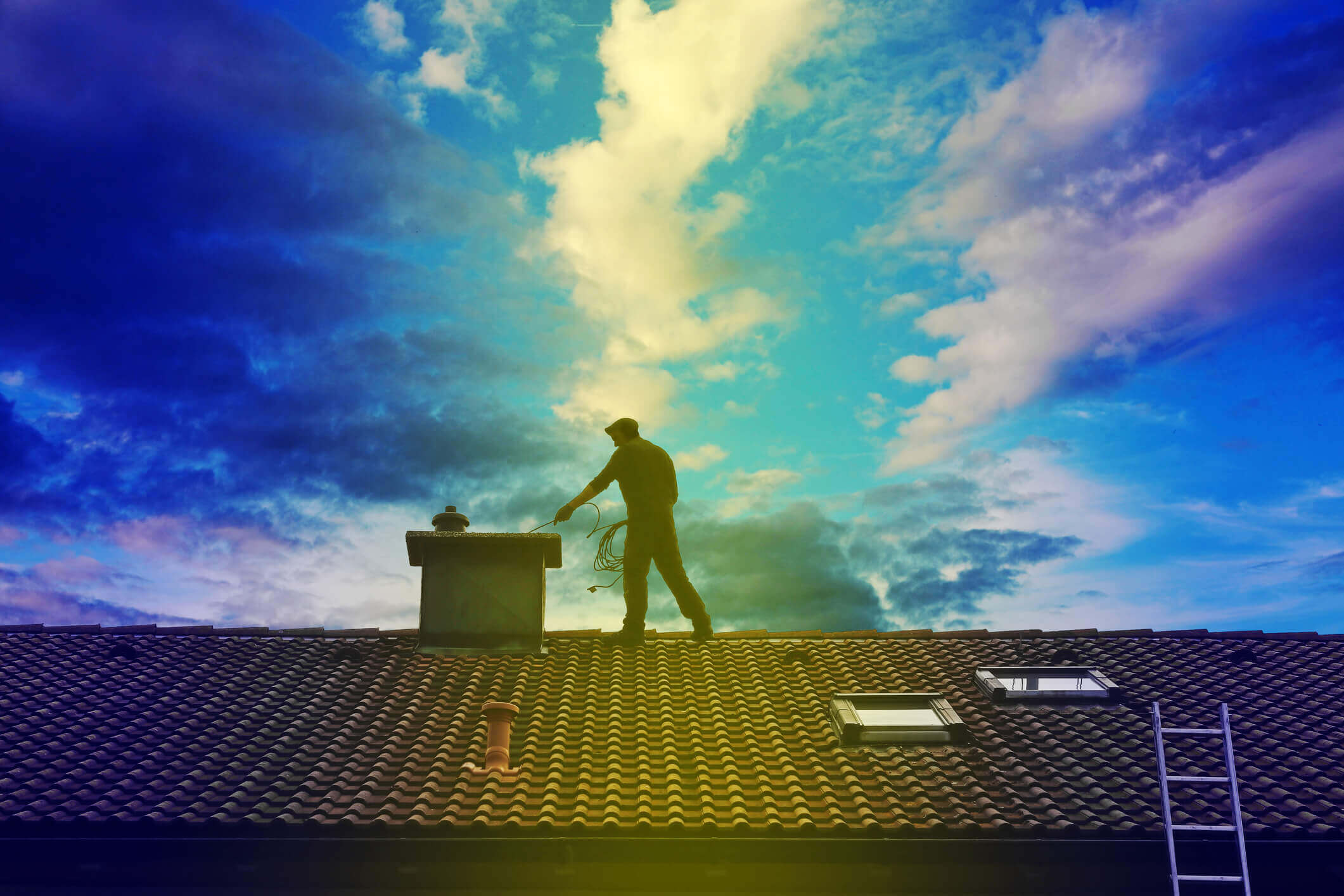 Chimney sweep silhouette working on rooftop against dramatic blue sky with clouds